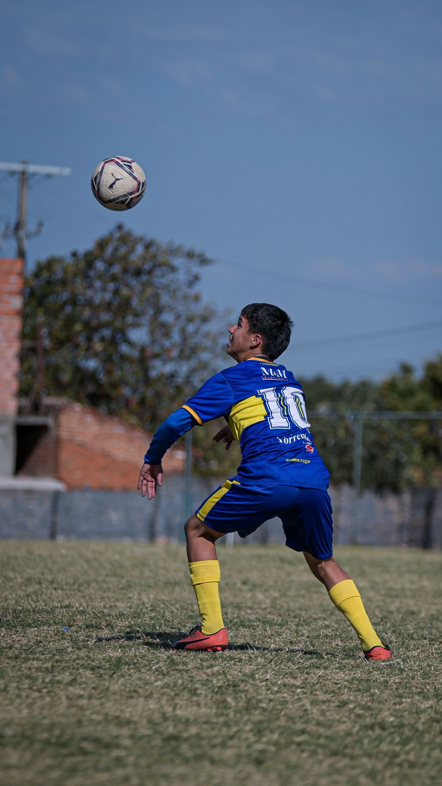 A young soccer player in blue and yellow gear focuses on heading the ball during a match.